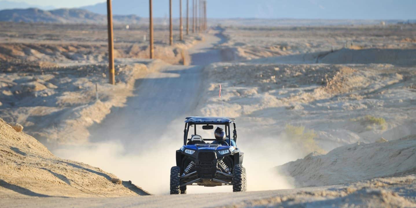 Two guests riding in ATV on a long dirt road