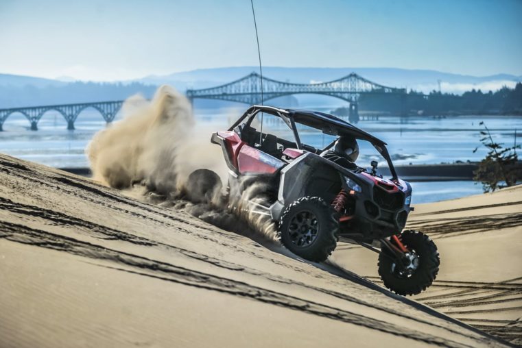 Riding an ATV through sand with a bridge in the background in Oregon
