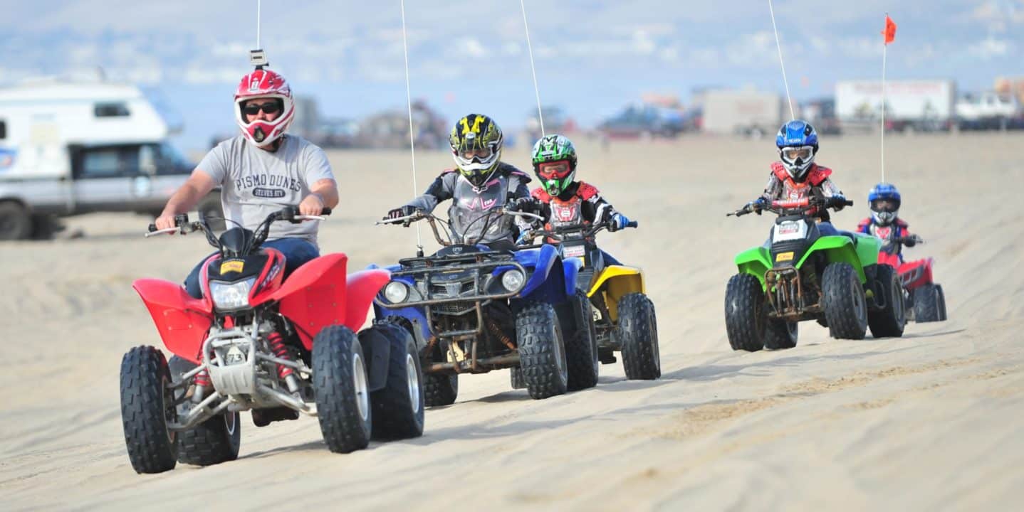 Family riding on different colored ATVs at Pismo Beach, CA