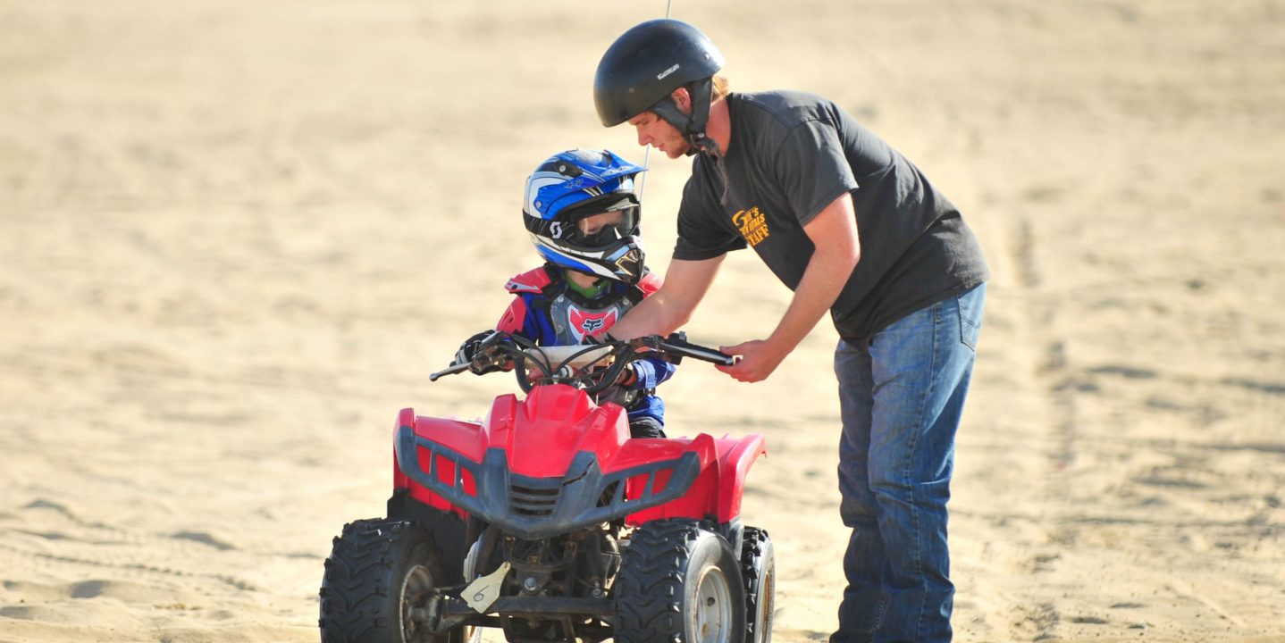 Adult teaching a child how to ride an ATV