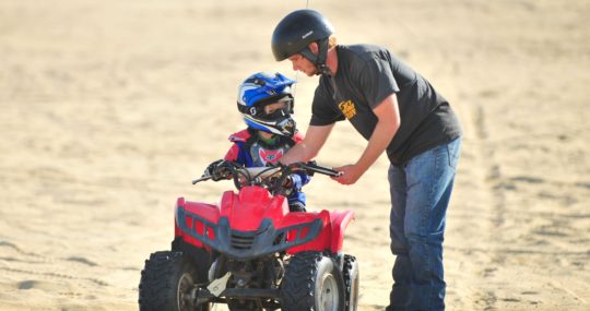 Adult teaching a child how to ride an ATV