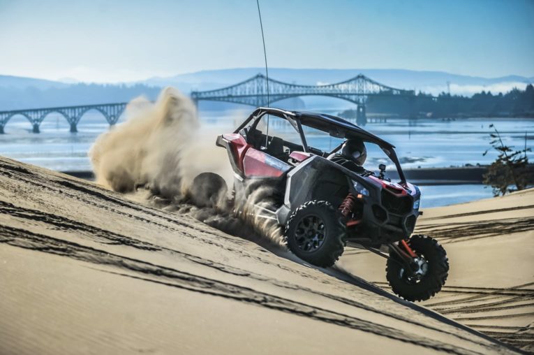 Riding an ATV through sand with a bridge in the background in Oregon