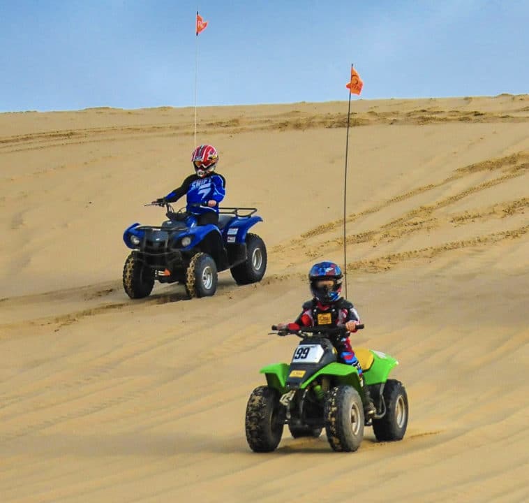 kids riding atvs through sandy dunes